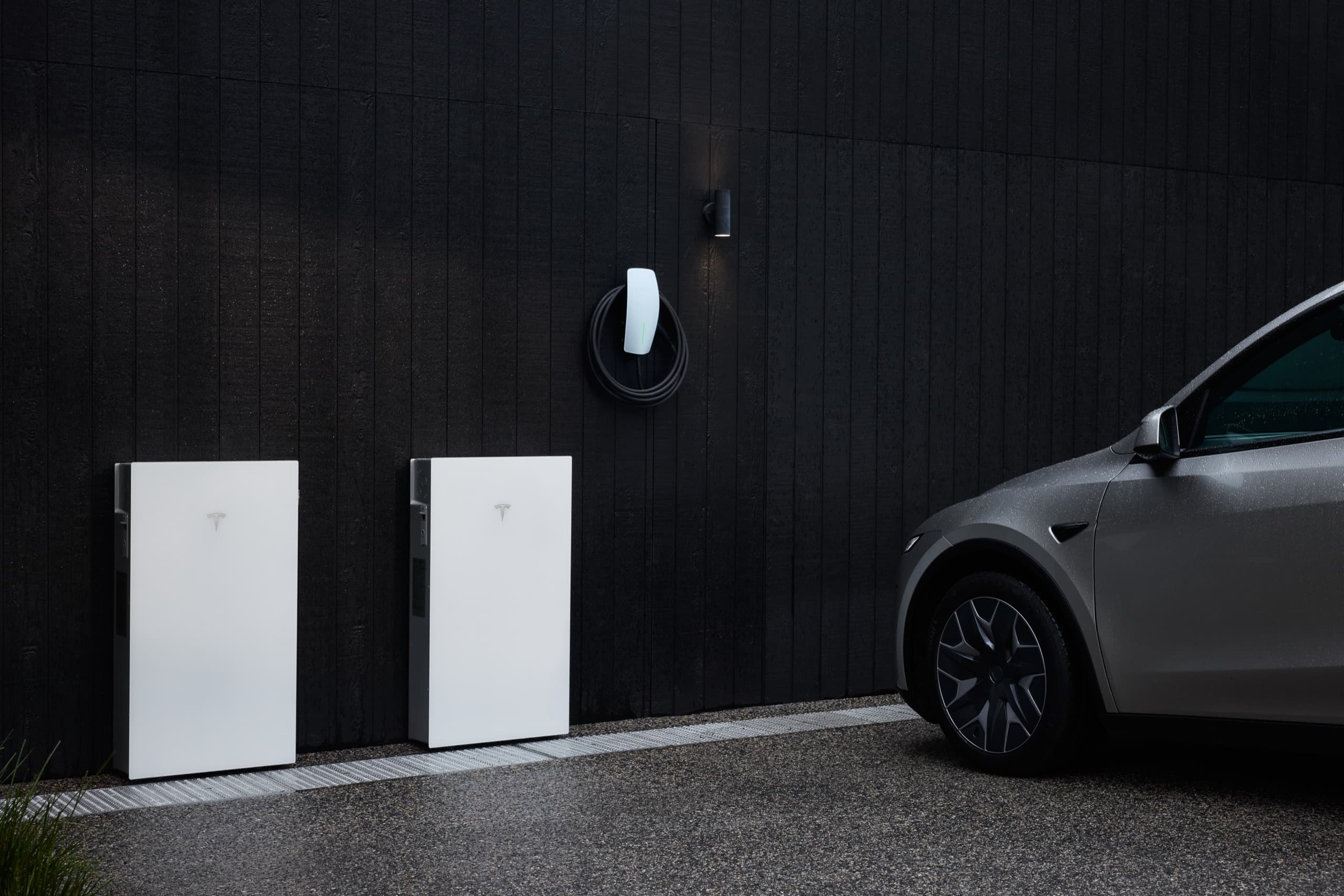 Tesla Wall Connector and Tesla Powerwall 3P units on a garage wall beside a parked Tesla