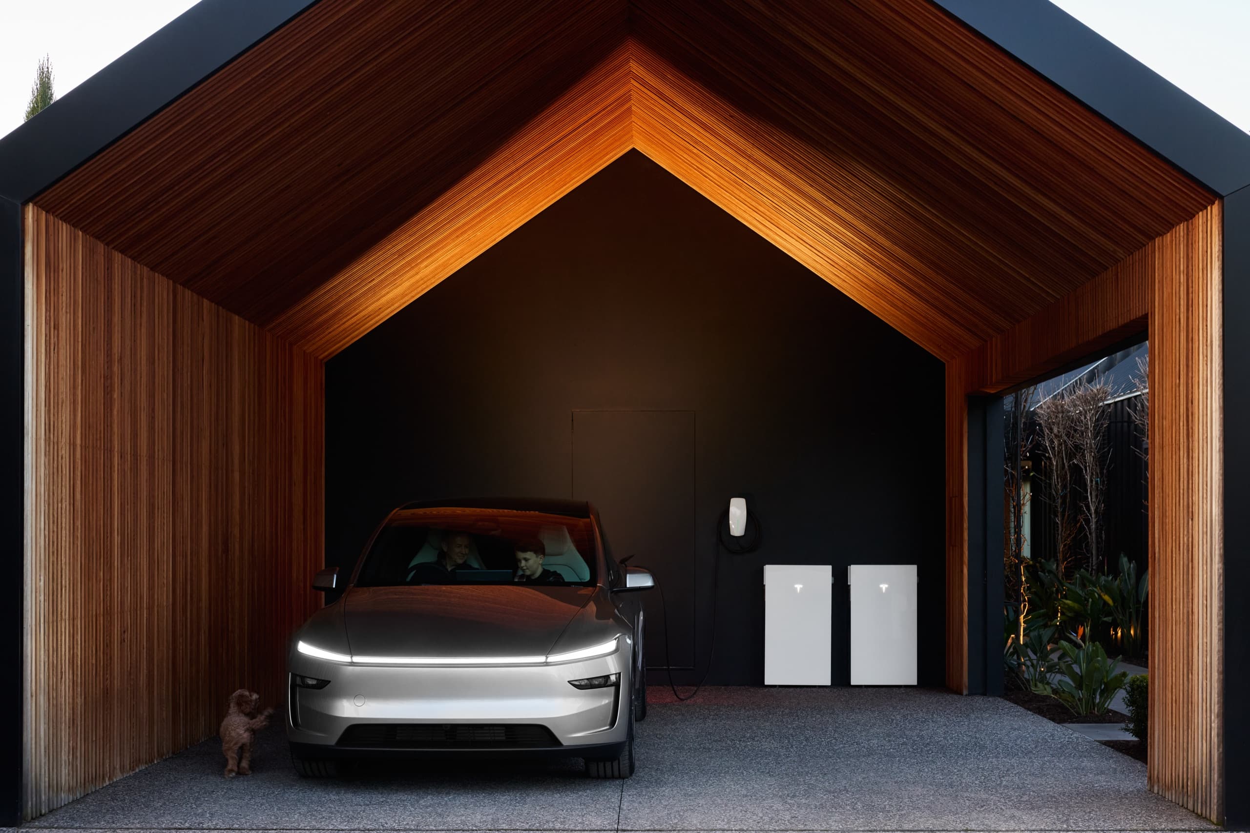 Tesla parked in a timber-lined carport with Tesla Powerwall 3P units on the back wall